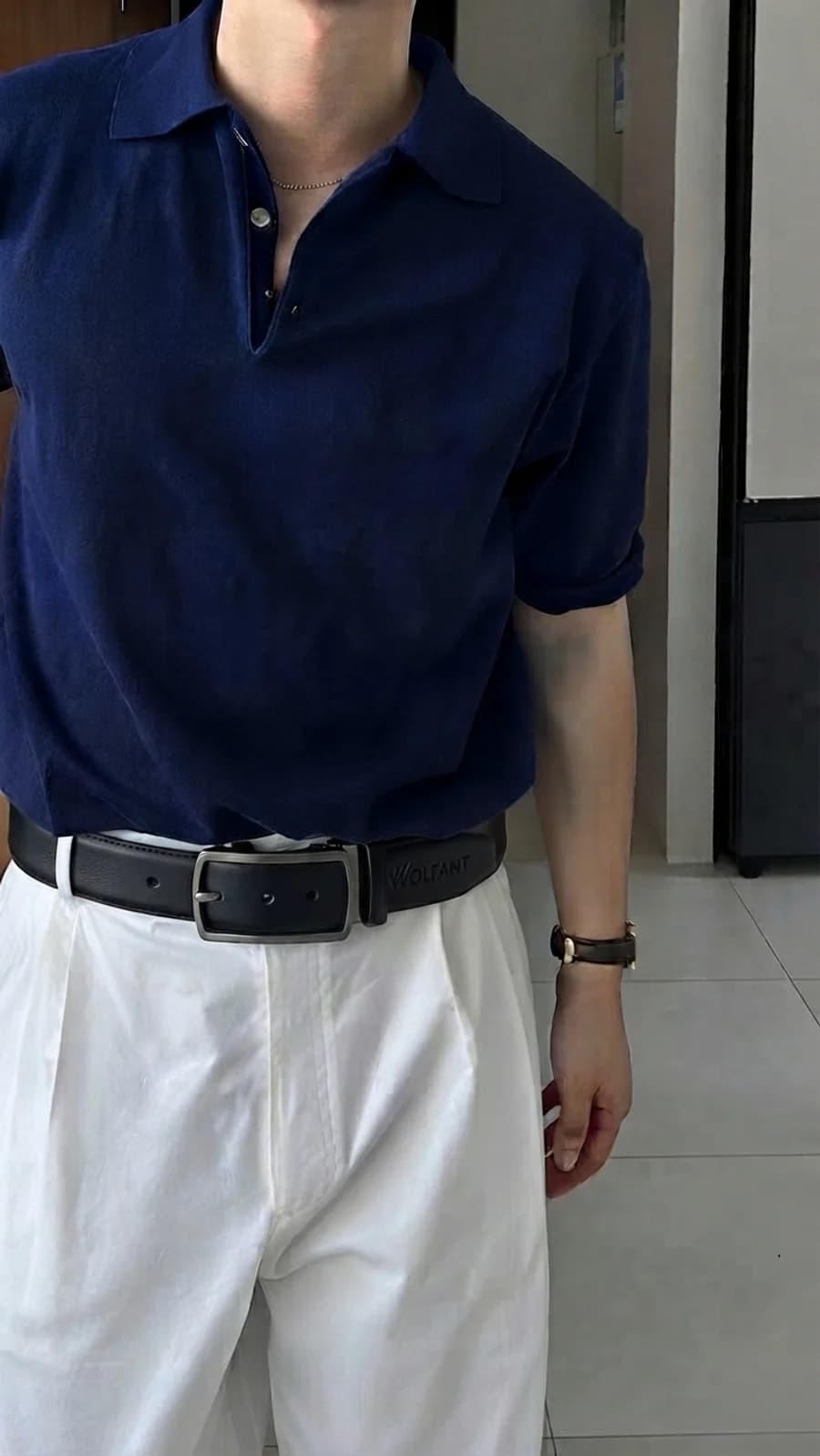 Men's black leather belt with white pleated trousers and a navy knit polo