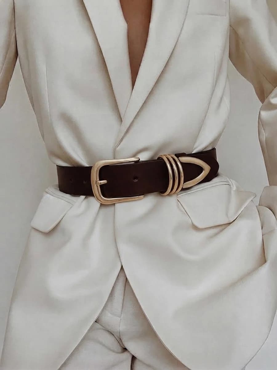 Women's wide dark brown leather belt with gold hardware cinching a cream blazer