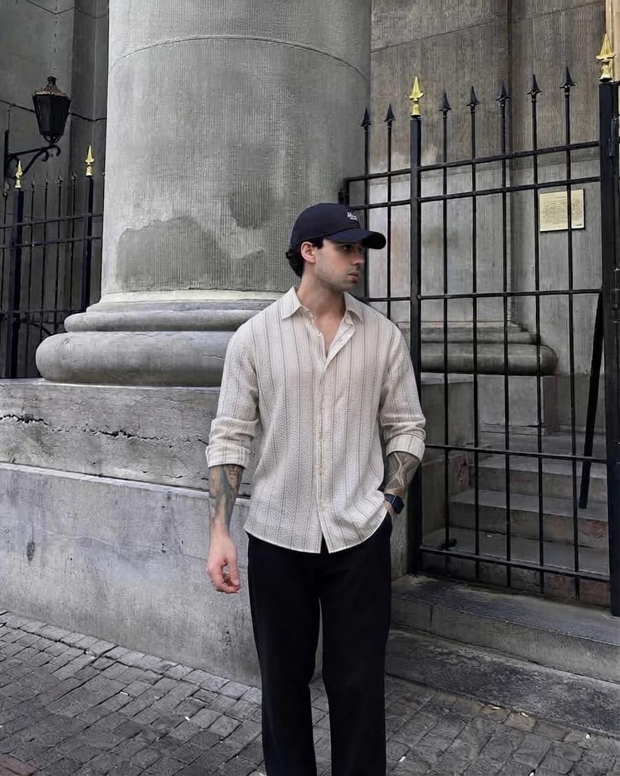 Men's spring outfit: striped cream shirt tucked into black trousers with a cap