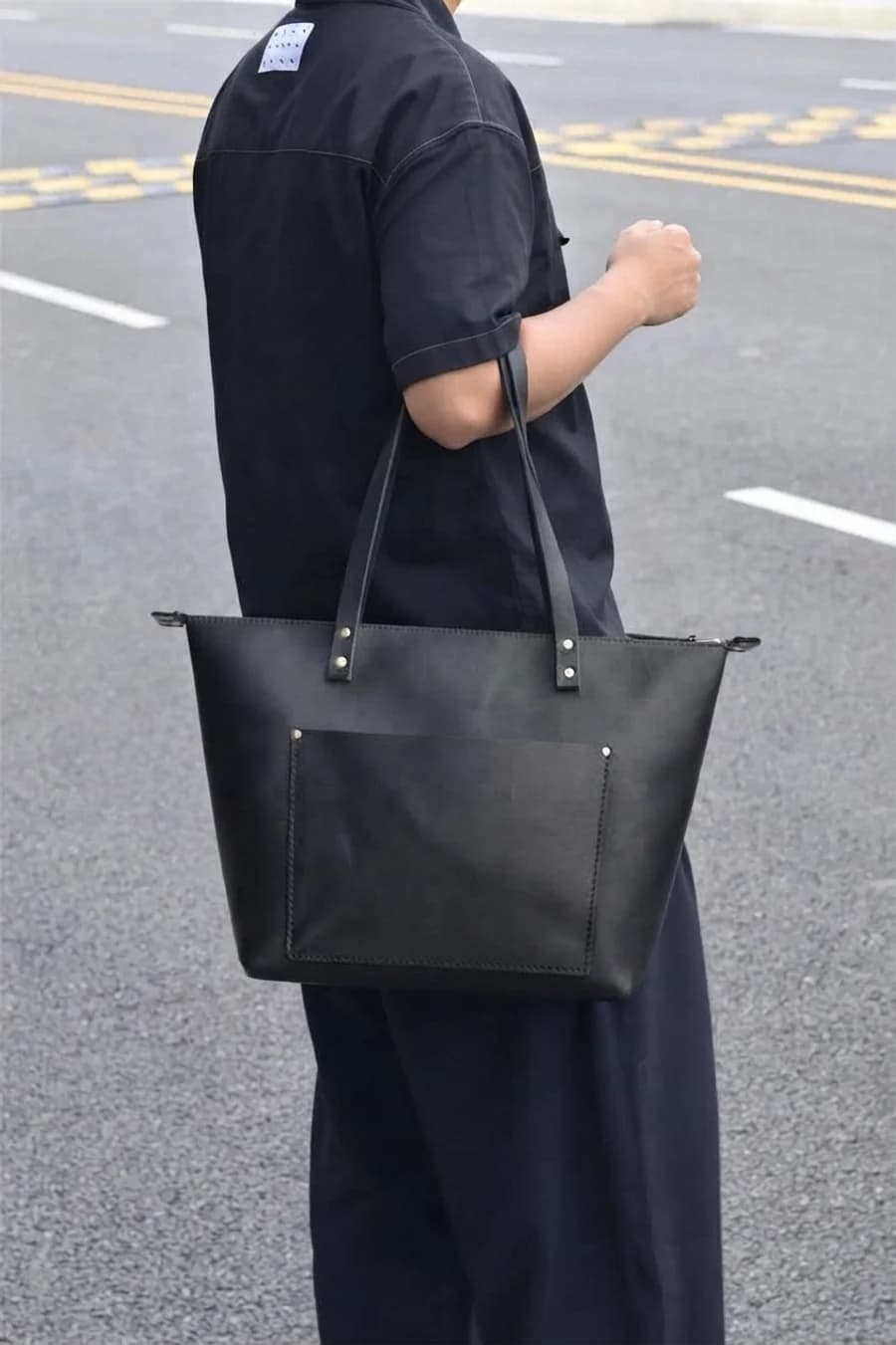 Men's black leather work tote with a front pocket worn over the shoulder