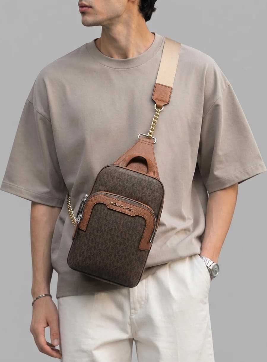 Michael Kors Hudson monogram sling pack with taupe t-shirt and cream trousers