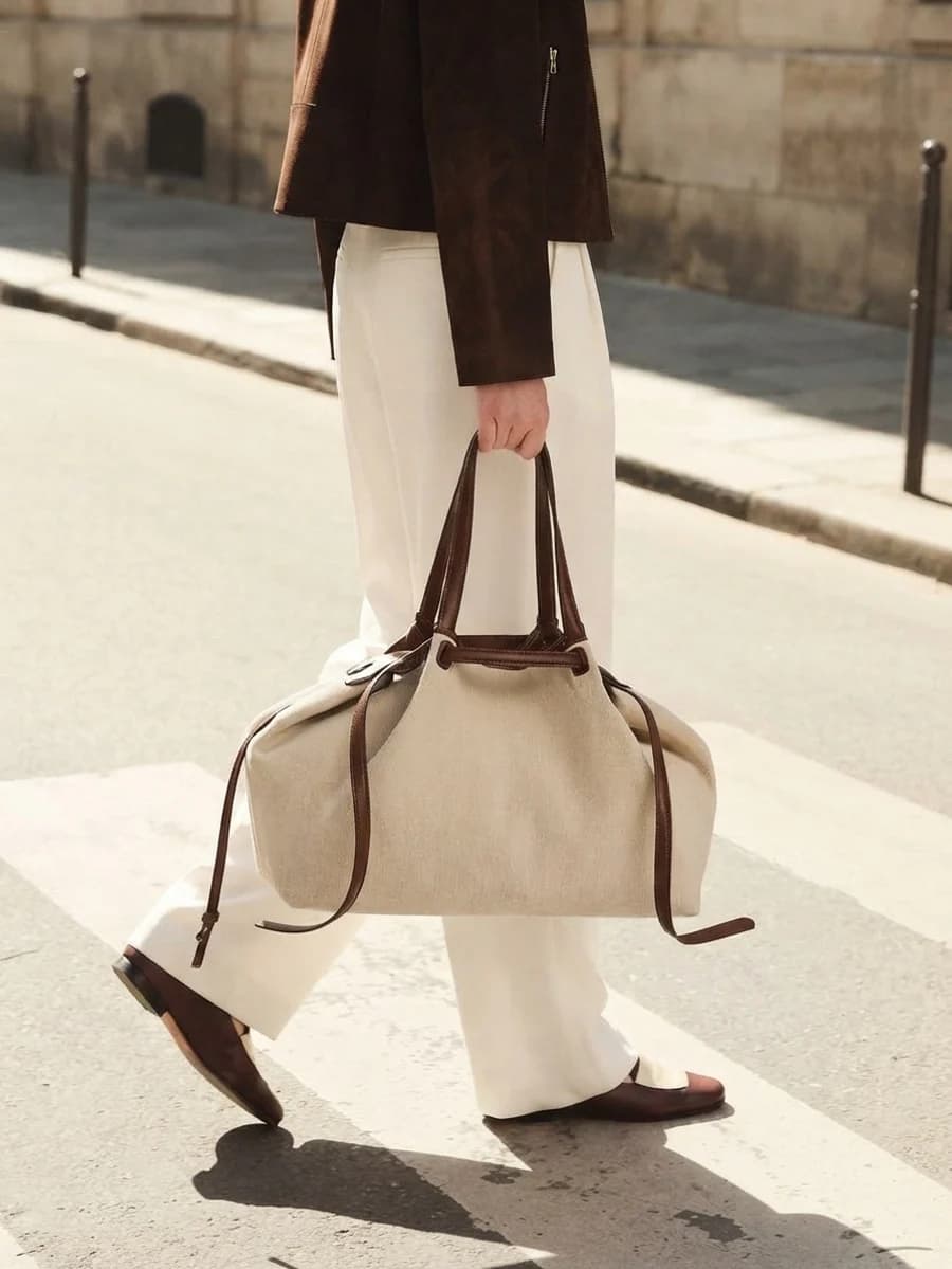 Large oatmeal canvas tote with brown leather handles and cream wide-leg trousers