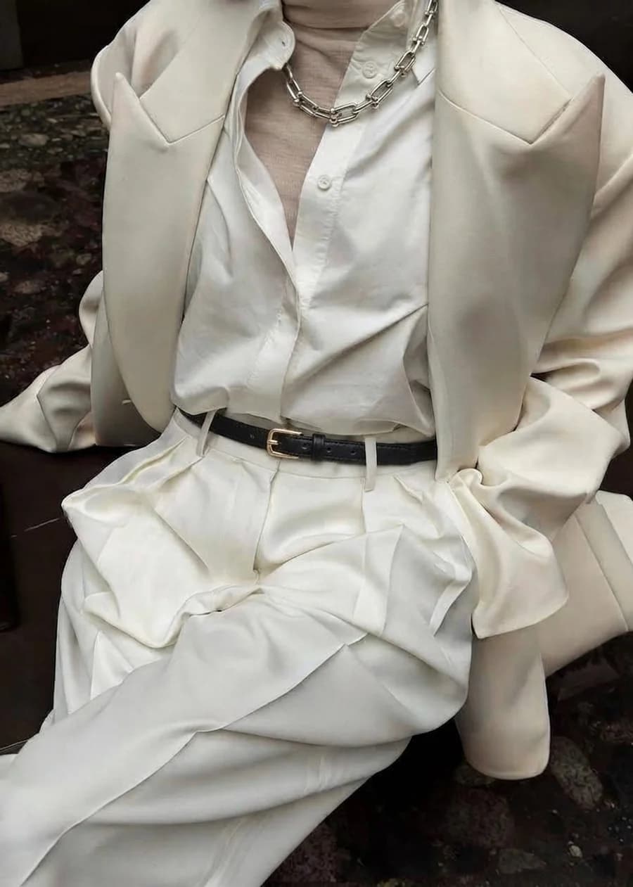 Women's slim black leather belt with a gold buckle worn with cream pleated trousers and a matching blazer