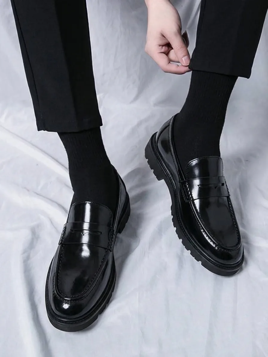Shiny black penny loafers with a lug sole, worn with black socks and black trousers