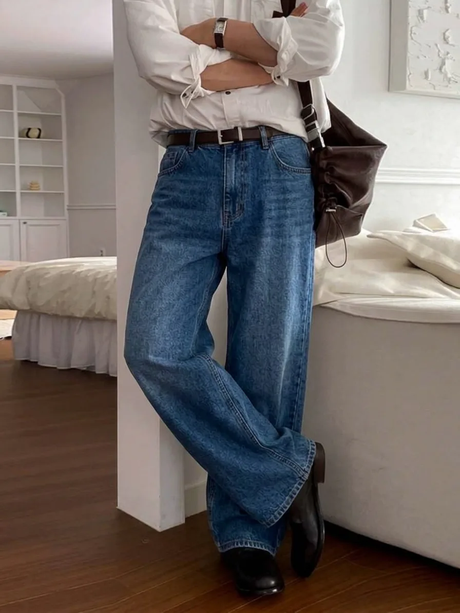 Medium-blue straight-leg jeans with a brown belt, a white shirt, and black boots