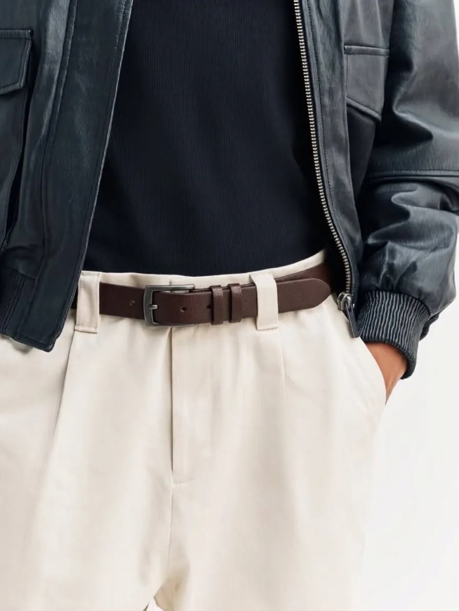 Brown leather belt with a rectangular silver-tone buckle, worn with cream pleated trousers