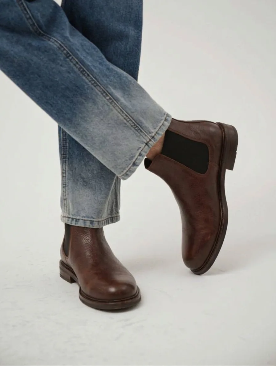Brown leather Chelsea boots with elastic side panels, worn with light-wash jeans