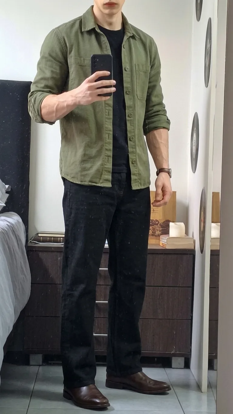 Man in an olive shirt worn open over a black T-shirt, with black jeans and brown boots