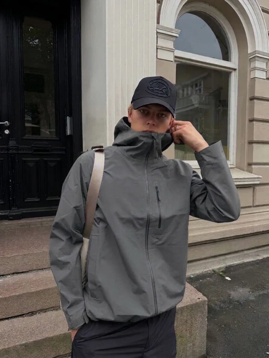 Grey hooded rain jacket worn with a black cap and black trousers