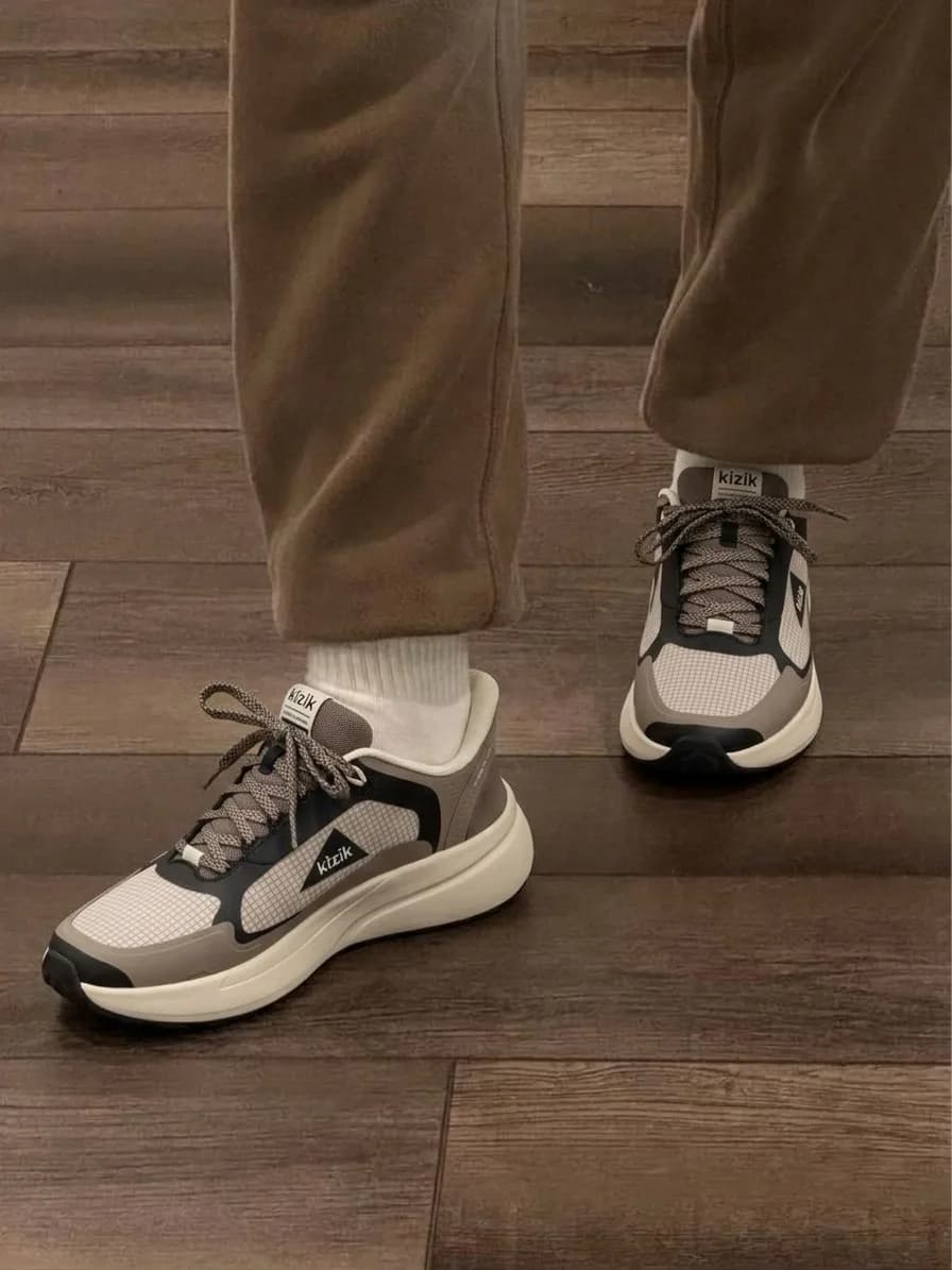 Grey and beige running shoes with a thick white sole, worn with brown trousers and white socks