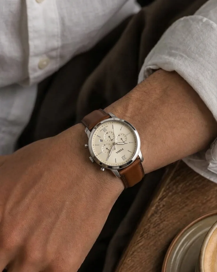 Silver-tone watch with a cream dial and a brown leather strap, worn with a light linen shirt