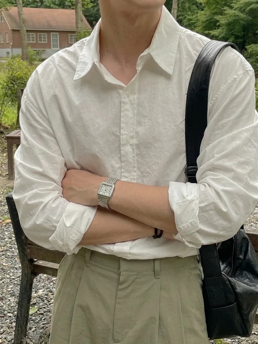 White button-down with rolled sleeves, worn with beige trousers, a metal watch, and a black bag strap