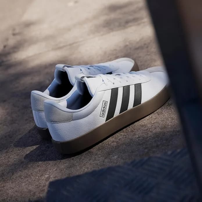 White leather sneakers with three dark side stripes and a gum sole