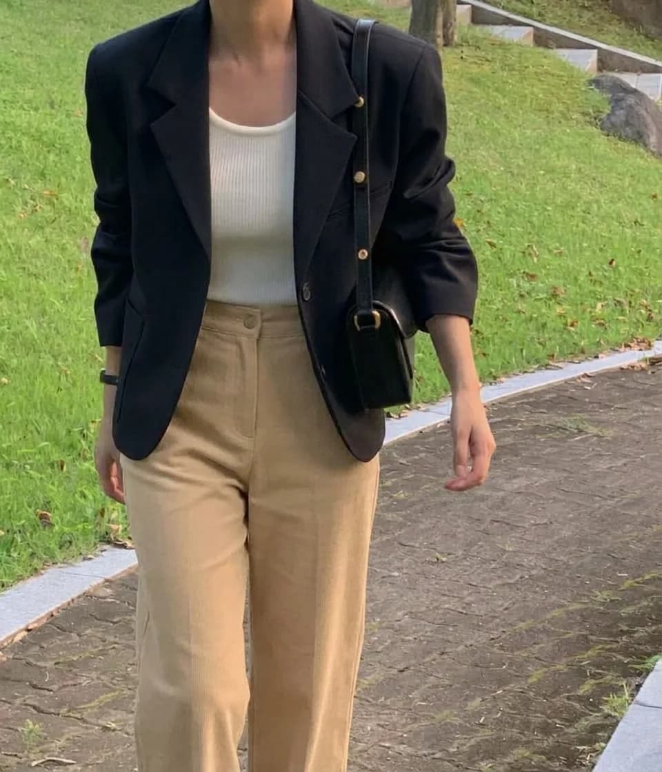 Black blazer with gold buttons over a white tank and beige trousers, with a small black bag