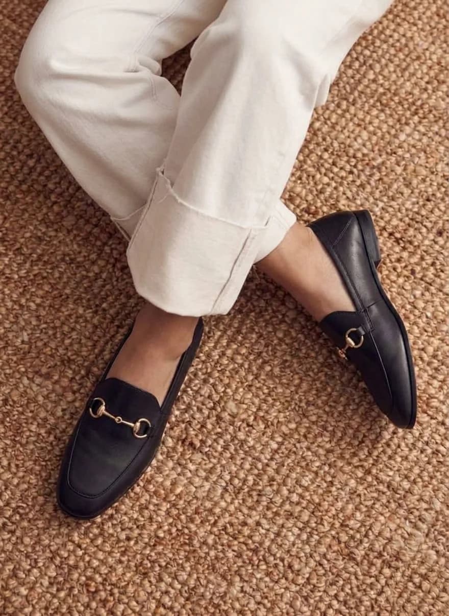 Black leather loafers with a gold horsebit, worn with cream trousers