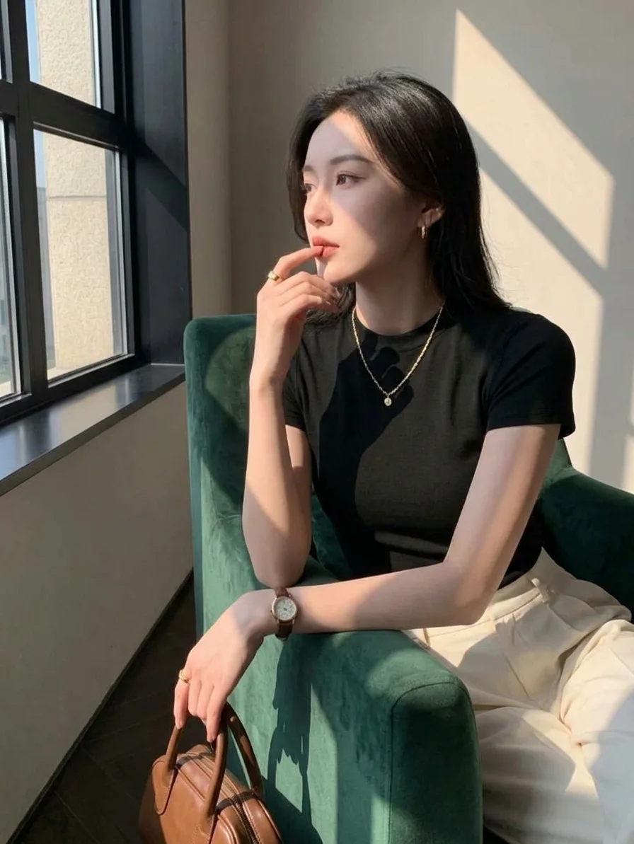 Woman in a black short-sleeve t-shirt and cream trousers, seated by a window