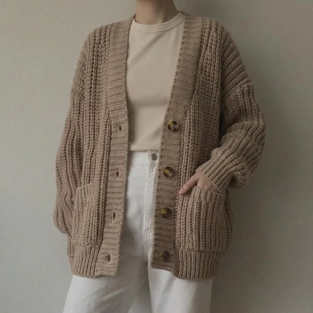 Beige chunky knit cardigan with large buttons over a cream top and white trousers