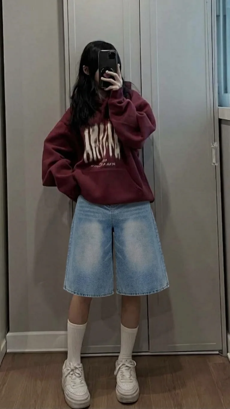 Light-wash denim bermuda shorts with white socks, sneakers, and a burgundy hoodie