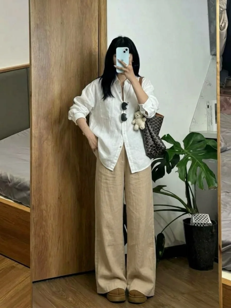 Woman in an oversized white button-down and beige wide trousers, taking a mirror photo