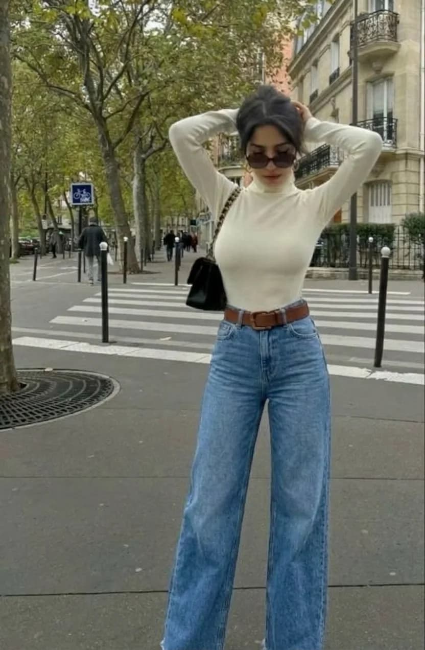 High-waisted wide-leg blue jeans with a brown belt and a cream turtleneck
