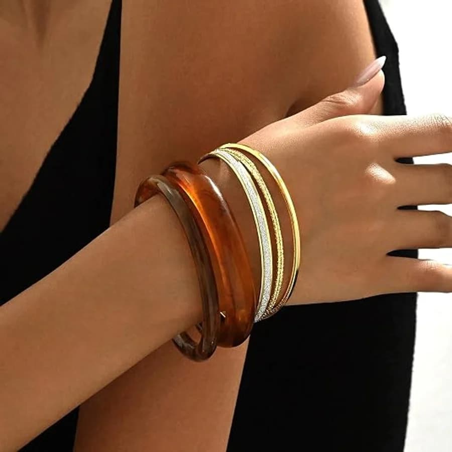 Stacked amber resin and metallic bangles on a wrist against a black top