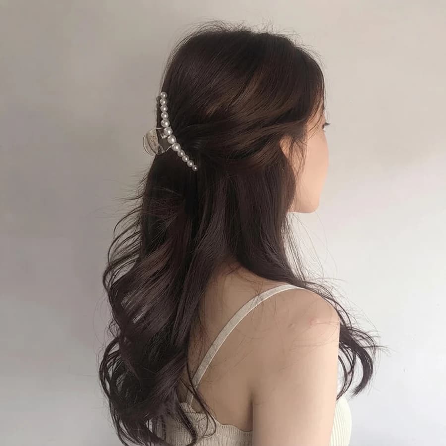 Pearl-embellished hair claw clip securing a half-up wavy hairstyle