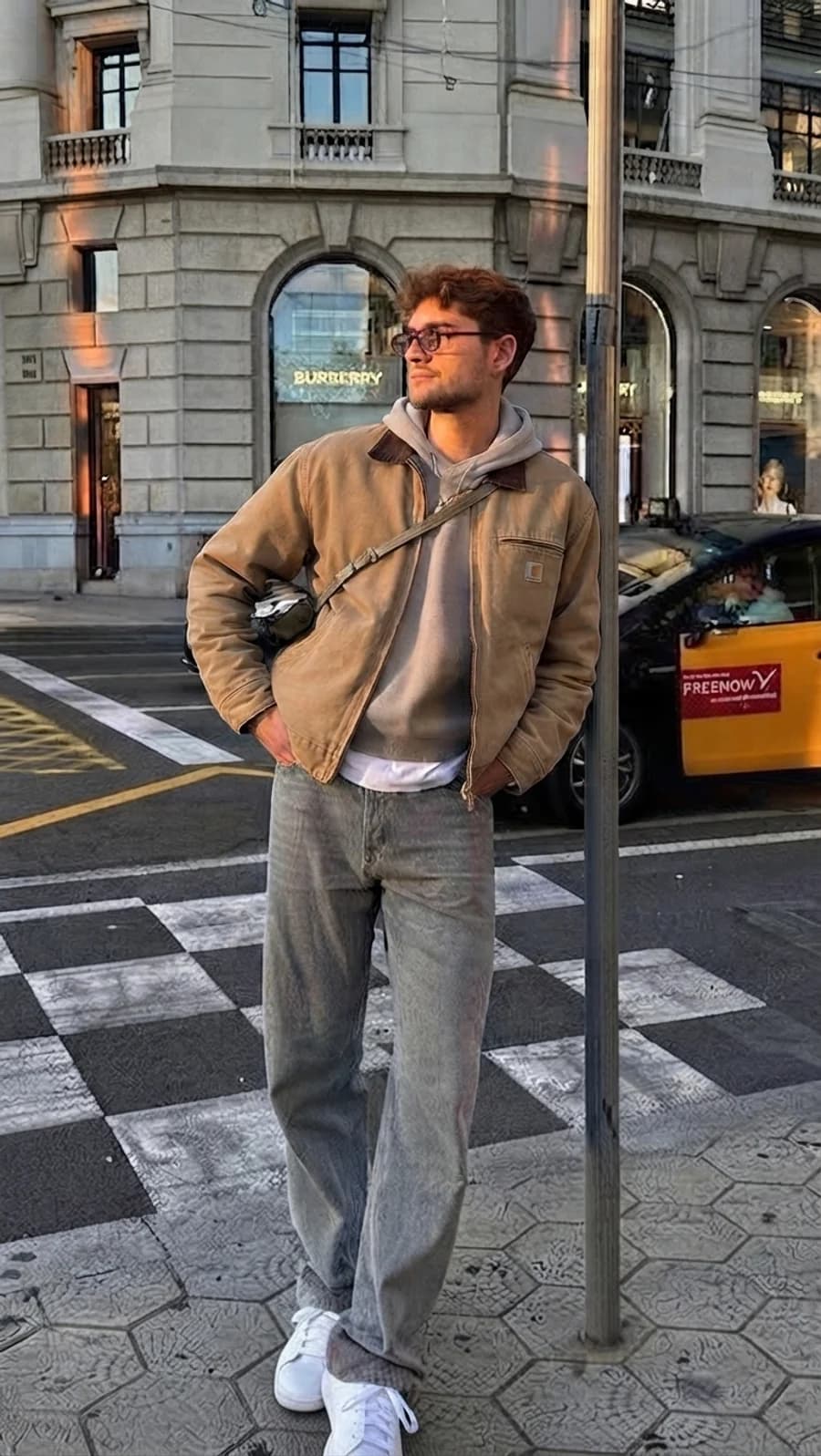 Mature streetwear: tan work jacket over a grey hoodie with straight light-wash denim and white sneakers