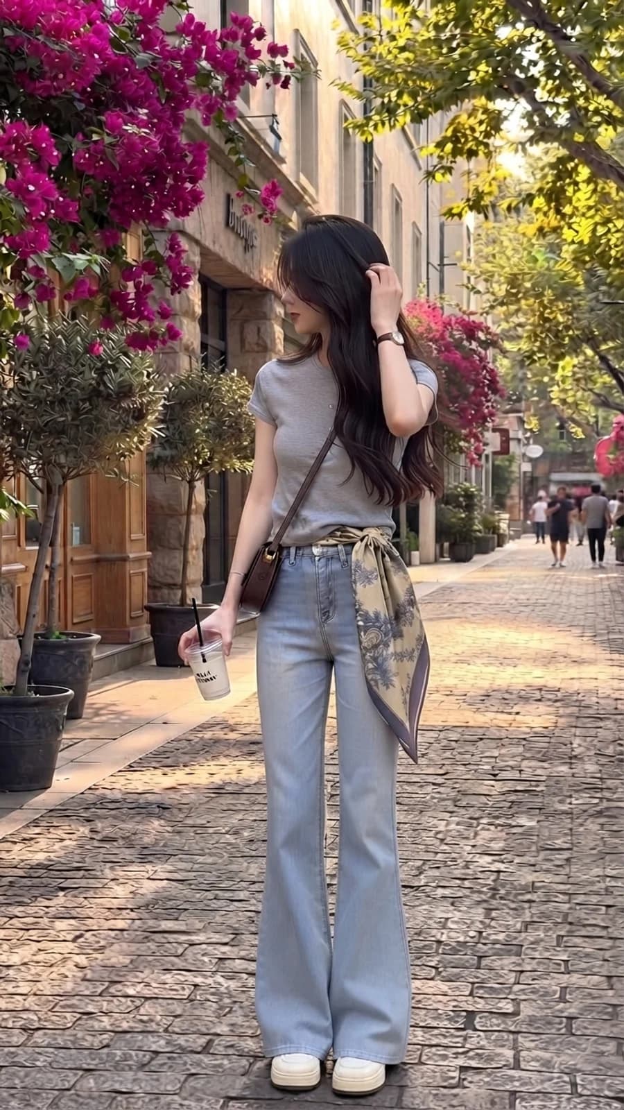 Women's summer outfit: grey tee tucked into light-wash flare jeans with a waist scarf