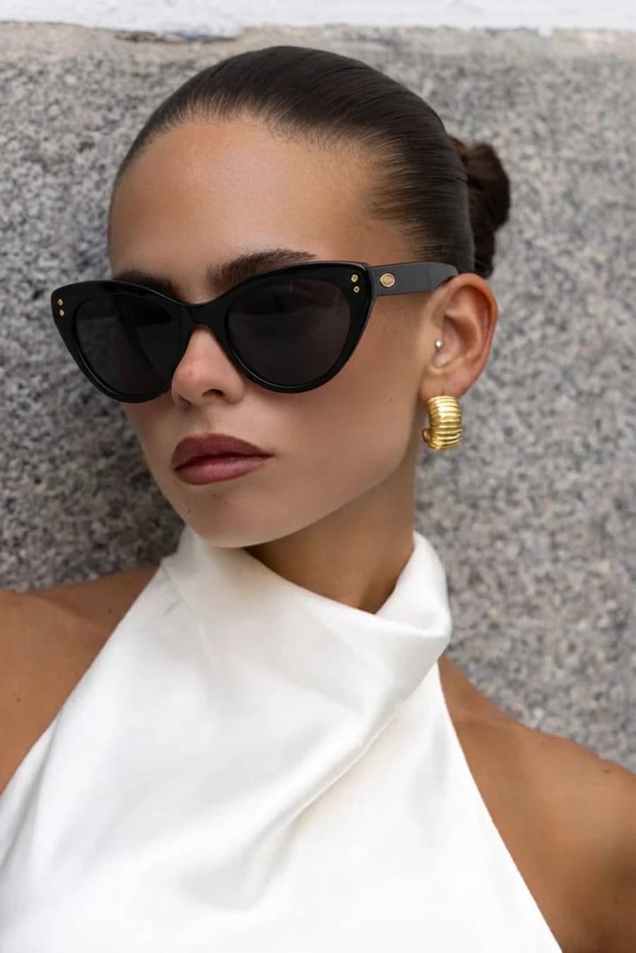 Women's black cat-eye sunglasses with gold studs, white halter top and gold hoop earrings