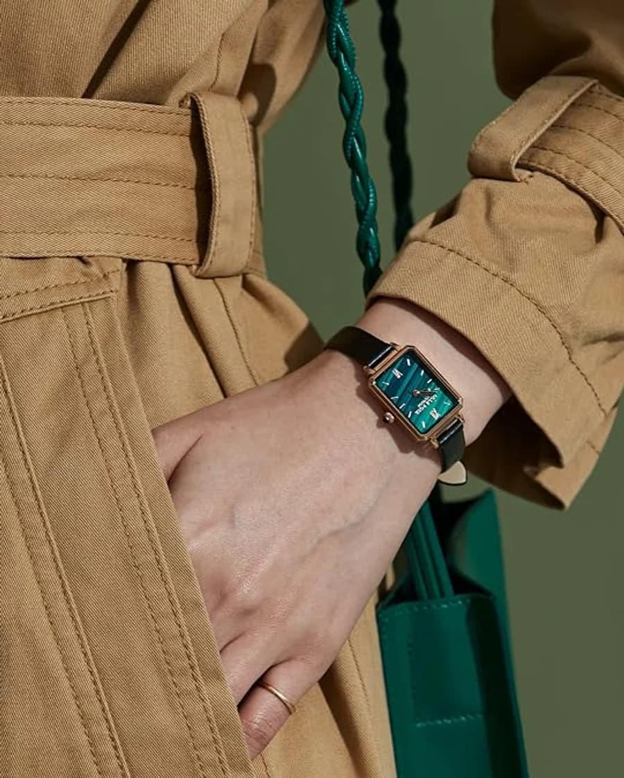 Rectangular green malachite dial watch with a black strap, worn with a camel trench coat and green bag