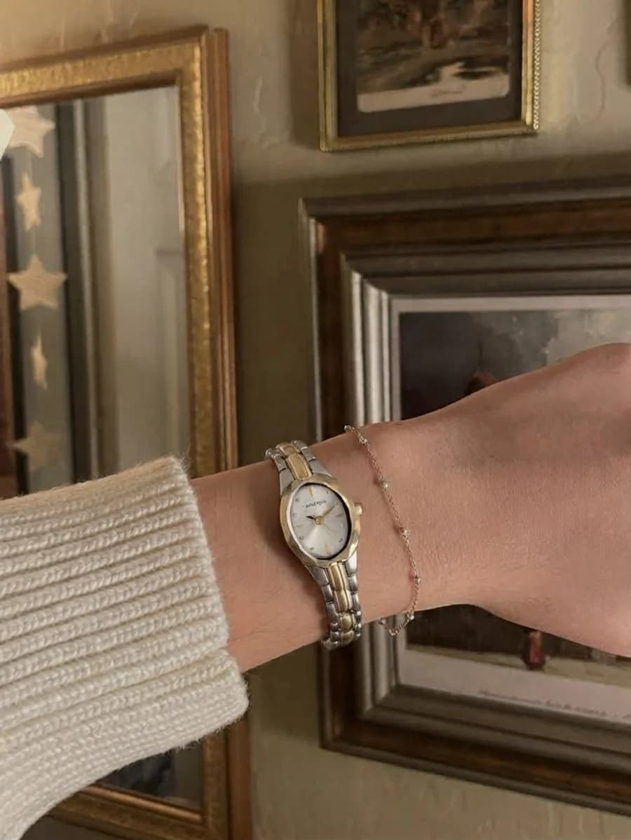 Women's two-tone gold and silver oval watch worn with a cream ribbed sweater and a fine gold bead chain